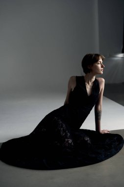 Siyah gece elbisesi giymiş sofistike bir kadın minimalist stüdyoda hafif ışıklandırmayla fotoğraflandı.