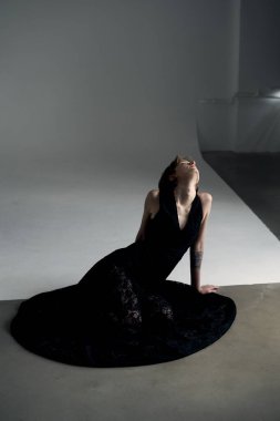 Siyah elbiseli kadının dramatik portresi. Aydınlanmış stüdyo ortamında zarif bir şekilde yerleştirilmiş.