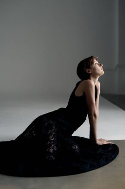 Dramatik yan ışıklandırması olan akışkan siyah elbiseli bir kadının sanatsal stüdyo portresi.