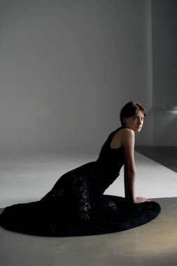 Siyah giysili zarif bir kadın, sanatsal bir pozda, minimalist stüdyo mimarisi ile yakalanmış.