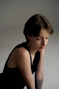 Siyah kolsuz bluzlu genç bir kadın sıcak stüdyo ışıklarıyla dikkatlice aşağıya bakıyor.