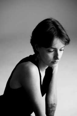 Siyah-beyaz kadın portresi kolsuz üstsüz, aşağıya bakan bakışlı ve sanatsal gölgeli.