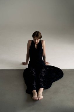 Siyah kıyafetli çağdaş dansçı sanatsal stüdyo ışıklandırmasında zarifçe oturuyor.