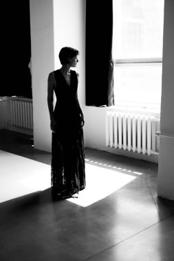 Uzun siyah elbiseli kadın silueti dramatik pencere ışığı kompozisyonunda yakalandı.