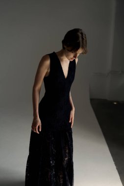 Siyah gece elbisesi giymiş bir kadın, düşünceli bir şekilde stüdyo ışıklarıyla aşağıya bakıyor.