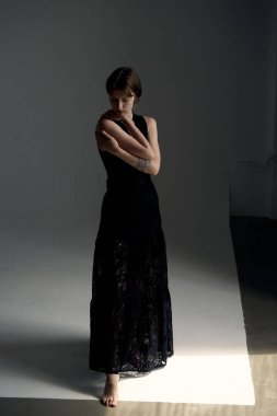 Dalgalı siyah elbiseli genç kadın dramatik stüdyo ışıklarıyla kendini kucaklıyor.