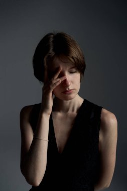 Elleriyle gözlerini kapayan genç kadın dramatik ışıklandırmayla yakın plan duygusal portreye bürünmüş.