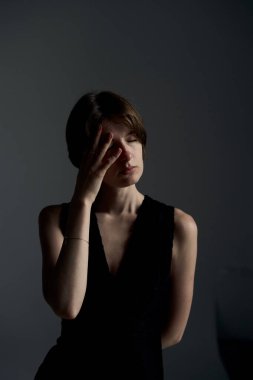 Siyah elbiseli genç kadın elleri ile yüzünü kapatıyor. Gri arka plana karşı utanç ve utanç ifade ediyor.