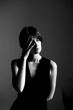 Dramatik siyah beyaz kadın portresi kolsuz üstsüz, iki eli de duygusal bir jest içinde saklanıyor.