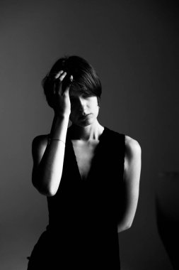 Düşünceli el hareketi ve ciddi ifade ile siyah elbiseli genç bir kadının monokrom stüdyo portresi