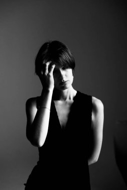 Kolsuz bluzlu, stüdyo ortamında alnına yakın duran siyah beyaz kadın portresi.