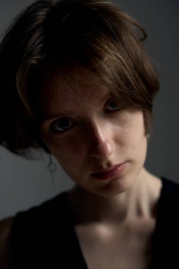 Kısa sarı saçlı ve dramatik yan ışıklandırmalı gölgeler yaratan yakın plan genç bir kadın portresi.