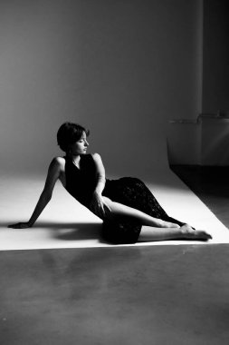 Tek renkli stüdyo fotoğrafı. Koyu renk elbiseli, geometrik mimari aydınlatma elementleri olan bir kadın.