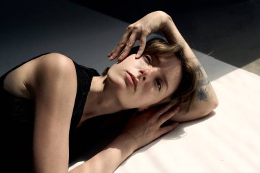 Sarışın, elleri başının arkasında uzanmış genç bir kadının samimi portresi.