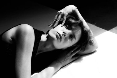 Elleri kafasının arkasında dalgın dalgın duran sanatsal siyah beyaz bir kadın.