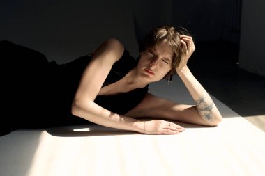 Düşünceli bir kadının sanatsal çıplak portresi stüdyo zemininde dramatik yan ışıklandırmada oturuyor.