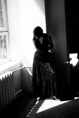 Siyah elbiseli kadının sanatsal silueti pencerenin yanında güçlü kontrastlı aydınlatma ve gölge desenli