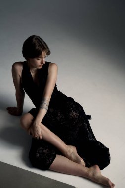 Genç bir kadının modern portresi. Kısa siyah saçlı, siyah bluzlu, oturduğu yerde.