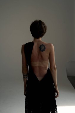 Tarafsız stüdyo arkaplanına karşı duran siyah arkalı zarif bir kadın sofistike moda fotoğrafçılığı sergiliyor.