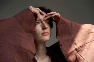 Burgundy blazer ceketli bir kadının sanatsal portresi. Elleri zarif bir şekilde yüzünün yakınına yerleştirilmiş.