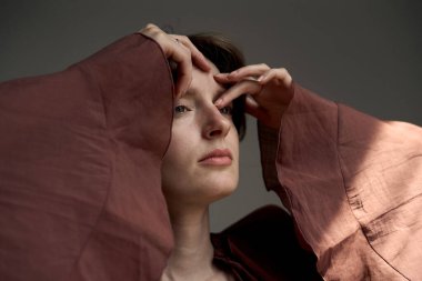 Sanatsal stüdyo ışıklandırmasında elleri çerçeveli, bordo ceketli kadının etkileyici portresi.