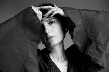 Akan gömlekli, elleri başının arkasına yerleştirilmiş dramatik gölgeler yaratan tek renkli kadın portresi.