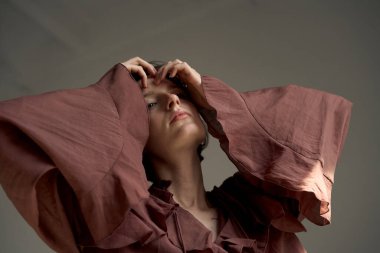 Terracotta gömlekli, zarif el hareketi ve yumuşak doğal ışıklandırmalı bir kadının sıcak stüdyo portresi.