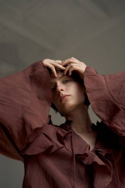 Pas rengi, büyük beden gömlekli, elleri başının arkasına yerleştirilmiş bir kadının sıcak stüdyo resmi.