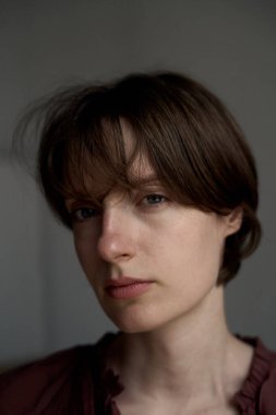 Kısa kahverengi saçlı ve doğal makyajlı yumuşak stüdyo ışıklandırmasında genç bir kadının yakın plan portresi.