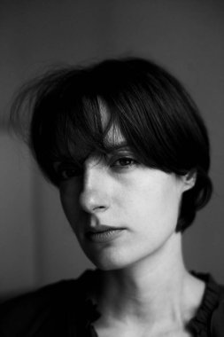 Kısa saçlı ve stüdyo ortamında derin düşüncelere dalmış genç bir kadının tek renkli portresi.