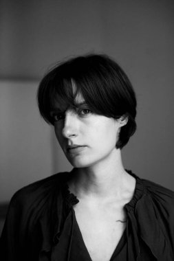 Kısa saçlı ve stüdyo ortamında derin derin bakan genç bir kadının tek renkli portresi.