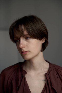 Genç bir kadının portresi, kısa kahverengi saçlı, pas rengi bluzlu, kibar ifadeli ve doğal ışıklandırmalı.