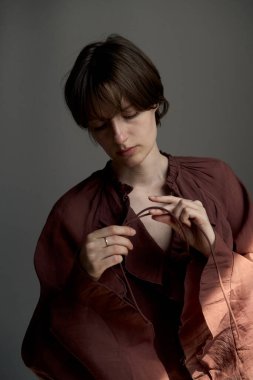 Pas rengi gömlekli kısa saçlı genç bir kadının moda portresi. Tasmayı ince bir el hareketiyle düzeltiyor.