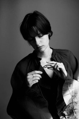 Kısa saçlı genç bir kadının tek renkli moda portresi stüdyo ortamında siyah gömlek yakasını düzeltiyor.