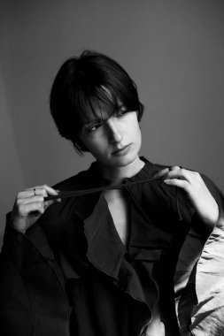 Perili genç bir kadının sanatsal siyah beyaz portresi dramatik stüdyo ışıklandırmasında koyu renk gömlek ayarlıyor.