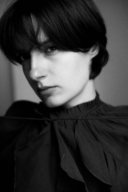 Karamsar siyah beyaz kadın portresi dramatik yan ışıklandırmada kısa siyah saçlı gölgeler ve dokuları vurguluyor.