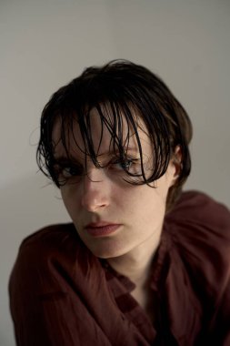 Burgundy kapüşonlu genç bir kadının düşünceli portresi aşağı bakan bakışları ve yumuşak stüdyo ortamında doğal saç dokusu.