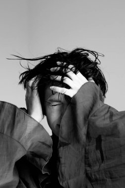 Düşünceli stüdyo ortamında eli saçı olan genç bir kadının sanatsal siyah beyaz portresi.