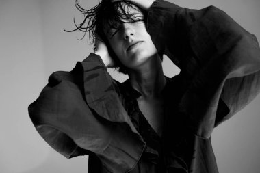 Siyah ceketli genç bir kadın. İki eli saçı olan. Kafasını dinamik stüdyo resmine geri atıyor.