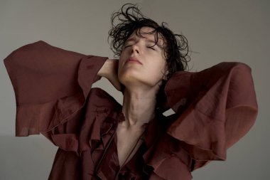 Burgundy blazer ceketli, elleri başının arkasında rahatlamış stüdyo portresi giymiş genç bir kadın.