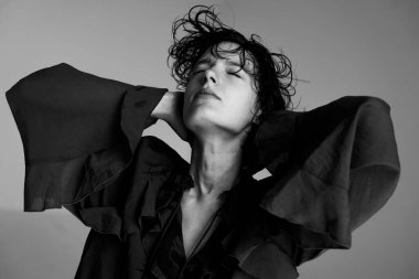 Tek renkli stüdyo portresi. Siyah ceketli, elleri başının arkasında, kendine güvenen bir kadın.