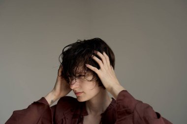 Burgundy blazer ceketiyle yüzünü kapatan genç bir kadın stüdyoda duygusal hassasiyet gösteriyor.