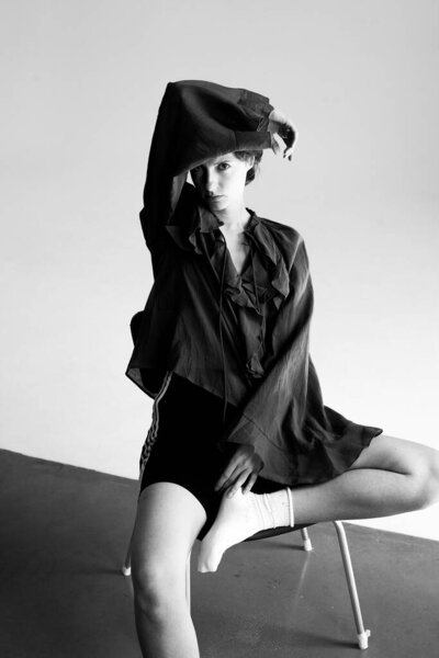 Contemporary fashion portrait of woman in black blazer and beret sitting elegantly on modern white chair