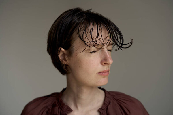 Портрет молодой женщины в бургундской одежде с натуральными взъерошенными волосами и боковым освещением создает пространственную студийную атмосферу