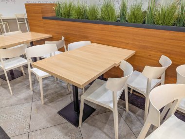 Beyaz ahşap masaları ve sandalyeleri olan modern açık hava yemek terası doğal bahçe manzaralı şık bir fresk restoranı oturma alanı yaratıyor. Yüksek kalite fotoğraf