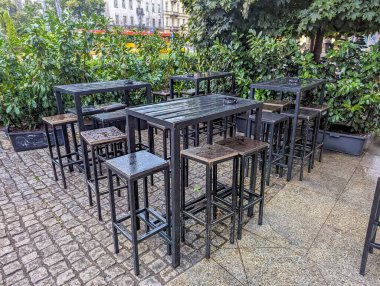 Açık terastaki beyaz yuvarlak masaların etrafına siyah metal sandalyeler yerleştirilmiş restoran verandası mobilyaları düzenleme. Yüksek kalite fotoğraf