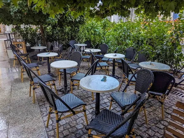 Açık hava restoranının terasında boş siyah metal sandalyeler ve doğal ışıklandırma altında beyaz yuvarlak masalar. Yüksek kalite fotoğraf