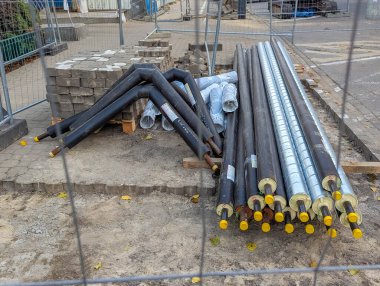 Sarı koruyucu kapaklı endüstriyel yalıtımlı ısıtma boruları ve aktif inşaat alanı altyapı projesinde depolanan siyah boru bölümleri. Yüksek kalite fotoğraf.