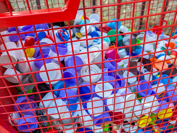 Abstract pattern created by multicolored plastic bottle caps collected inside red wire mesh heart-shaped container for recycling purposes. High quality photograph.