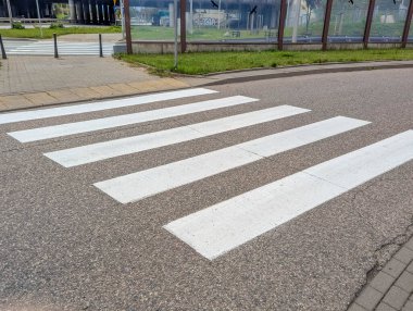 Empty pedestrian crosswalk with white stripes on asphalt road surface in quiet urban area during daytime. High quality photograph.
